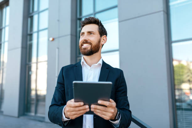 istock Happy confident millennial european man with beard in suit use tablet, look at empty space near modern office 1473016656