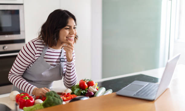 istock Happy young woman enjoying cooking at home, using modern laptop 1473017411