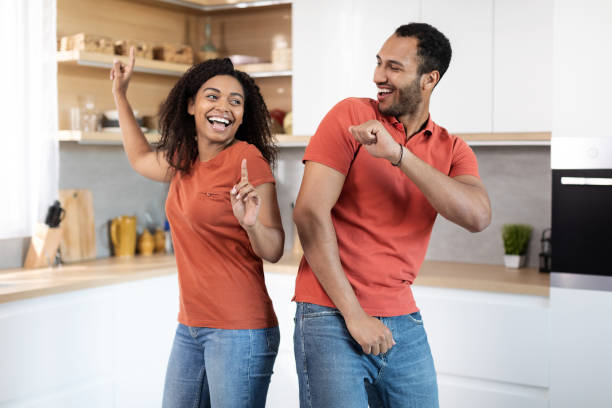 Happy young african american guy and woman in same t-shirts have fun and dance together Happy young african american guy and woman in same t-shirts have fun and dance together, celebrating move or anniversary in cozy kitchen interior. Couple enjoy free time at home, love and relationship two men same clothes stock pictures, royalty-free photos & images