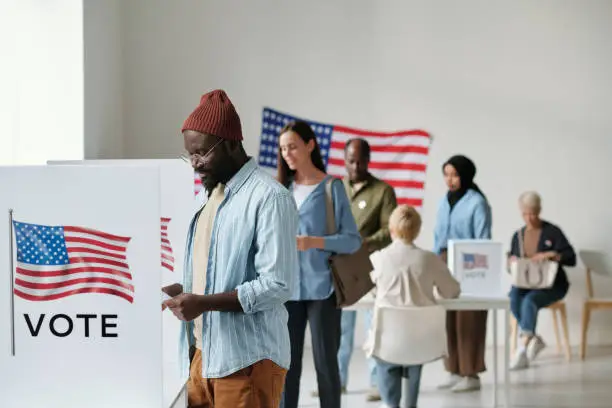 Photo of Group of young multicultural voters standing in queue in polling place