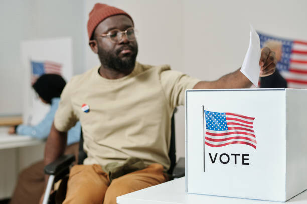 skrzynka na karty do głosowania na biurku i czarnoskóry mężczyzna z niepełnosprawnością dokonujący wyboru - vote casting zdjęcia i obrazy z banku zdjęć