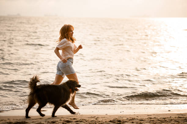 istock beautiful side view on woman running along sandy beach at water with her dog 1473018024