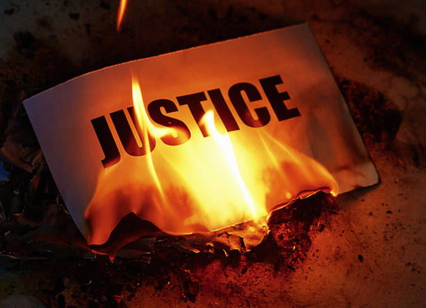 istock Justice being destroyed: word goes up in flames, representing injustice 1473019585