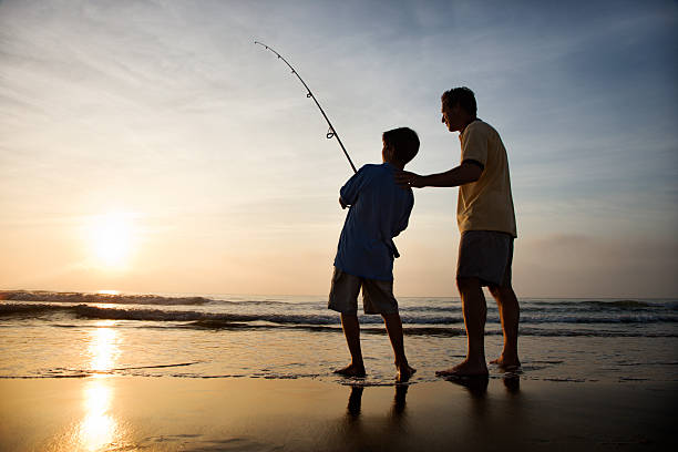 Man and young boy fishing in surf stock photo