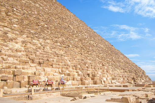 Pyramids of Giza, Giza Necropolis, Egypt - March 12, 2023: Egyptian man riding a camel at the Pyramids of Giza.\n\nThe Giza Necropolis is a large area near Giza, a suburb of Cairo that has many tombs and burial sites. It is also where you can find the famous Pyramids of Giza, the Great Sphinx, and more. The name comes from the ancient Greek word nekropolis, which literally means “city of the dead”.\n\nThe Giza Complex was once near the ancient Egyptian capital of Memphis, and the Giza plateau is where a number of pharaohs, queens, and nobles of the Fourth Dynasty of ancient Egypt were buried. \n\nAll three of Giza's pyramids and their elaborate burial complexes were built  from roughly 2550 to 2490 B.C. The pyramids were built by Pharaohs Khufu, Khafre, and Menkaure.