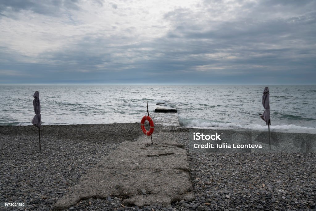 A deserted beach on the coast of Sochi and a lifebuoy on the pier against the background of a cloudy sky and stormy Black Sea, Adler, Krasnodar Territory, Russia Adler District Stock Photo