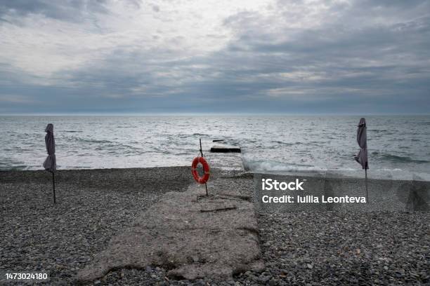 A Deserted Beach On The Coast Of Sochi And A Lifebuoy On The Pier Against The Background Of A Cloudy Sky And Stormy Black Sea Adler Krasnodar Territory Russia Stock Photo - Download Image Now