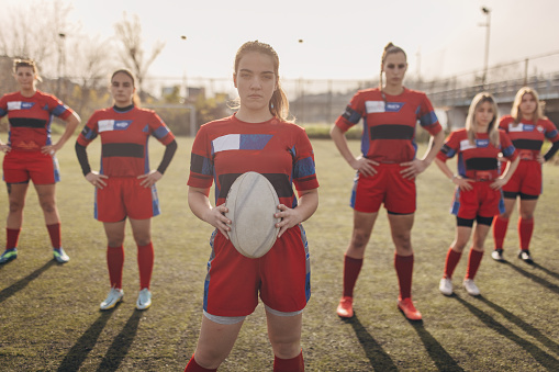 Group of women, female rugby team players standing on sports field outdoors together.