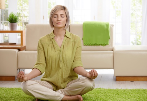 Woman sitting on floor at home doing yoga meditation.