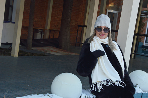 Young girl. Stylish, fashionable young woman in a white hat, dark fur coat scarf and sunglasses posing outdoors in cold weather.