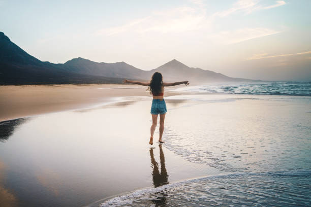 jeune femme marchant seule sur la plage au coucher du soleil - concept de liberté et de bonheur - shorts rear view summer beach photos et images de collection