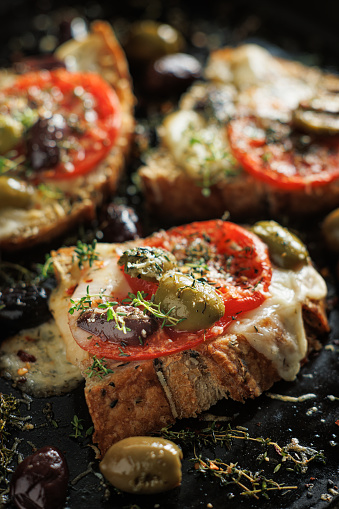 Grilled cheese toast with tomatoes and olives seasoned with thyme on a black background, close up