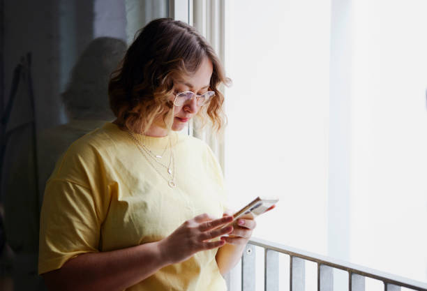 istock Woman standing by a window and using mobile phone at home 1473033809