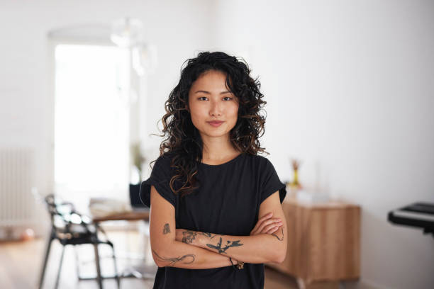 Portrait of a beautiful young asian woman standing in living room Portrait of a beautiful young asian woman in living room. Happy female looking at camera with arms crossed standing at home. black tattoo stock pictures, royalty-free photos & images