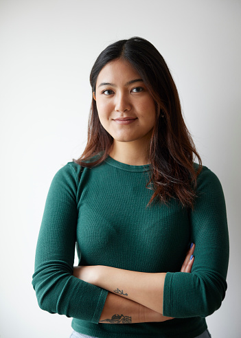 Portrait of beautiful asian woman standing confidently by white background. Asian female with arms crossed staring at camera against white wall.
