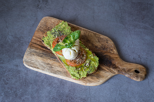 Top view of a toast with cheese, tomato and avocado served on a wooden surface