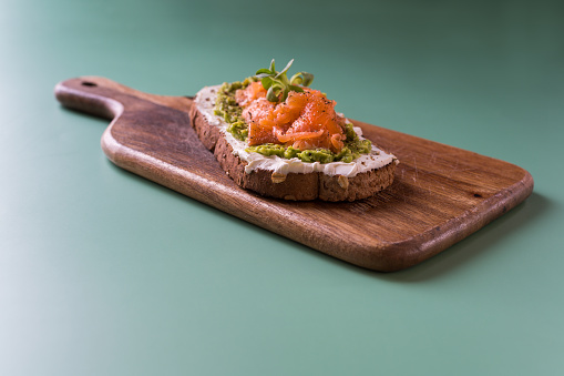 Toast with mayonnaise, avocado and salmon on top served on a wooden surface