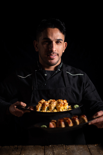 A portrait of a male sushi chef holding plates of sushi.