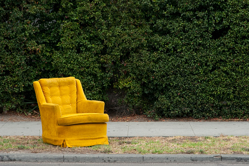 A yellow vintage chair sitting on the side of a street.