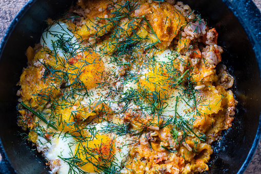 Boiled rice with fried eggs, pumpkin, peppers, carrots and onions in a cast iron pan, close up. Food background. Healthy food