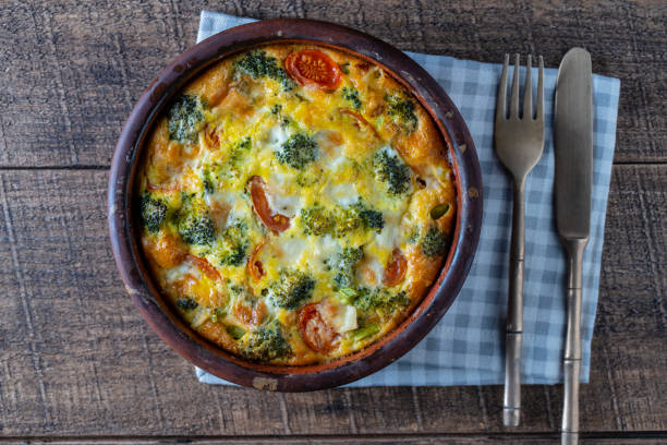 istock Ceramic bowl with vegetable frittata, simple vegetarian food. Frittata with egg, tomato, pepper, onion, broccoli and cheese on wooden table. Italian egg omelette 1473036353