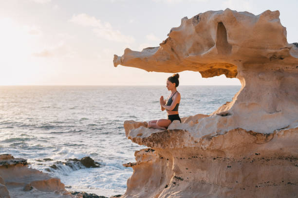 Young woman meditating on a cliff overlooking an ocean