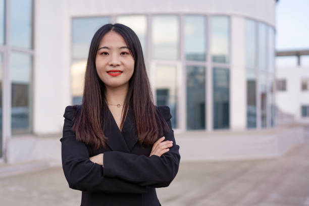 portrait d’une jeune femme d’affaires asiatique en costume regardant la caméra, souriante et debout contre la scène de la ville devant des immeubles de bureaux modernes - looking at camera one person urban scene photography photos et images de collection