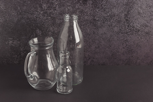 Colorless transparent glass bottles of a different shape and size and a glass pitcher on a dark background.