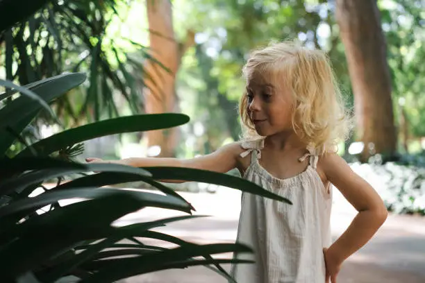 Photo of Cute caucasian pretty blonde two year old girl, toddler, kid exploring green plants in botanic garden.Nature and child concept.Half body shot