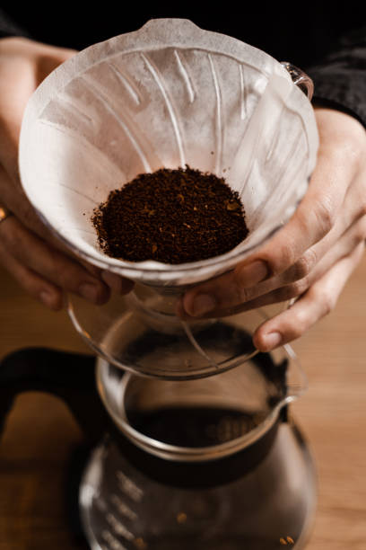 istock Barista holding pour over device with ground coffee on paper filter before pouring water from drip kettle. Process of brewing pour over filter coffee in cafe. 1473047246