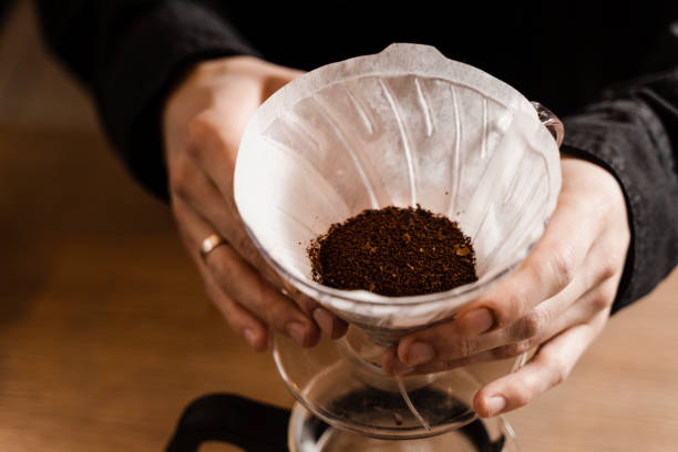 istock Barista holding pour over device with ground coffee on paper filter before pouring water from drip kettle. Process of brewing pour over filter coffee in cafe. 1473047247