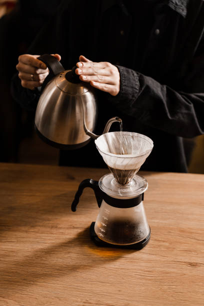 istock Pour over filter coffee alternative brewing method. Pouring hot water over roasted and ground coffee beans contained in paper filter. 1473047275