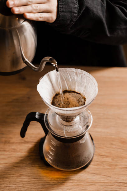 istock Pour over filter coffee alternative brewing method. Pouring hot water over roasted and ground coffee beans contained in paper filter. 1473047278