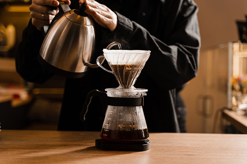 Drip filter coffee brewing. Barista pouring hot water over filter with ground coffee in the funnel. Pour over alternative method of pouring water over ground coffee beans contained in filter