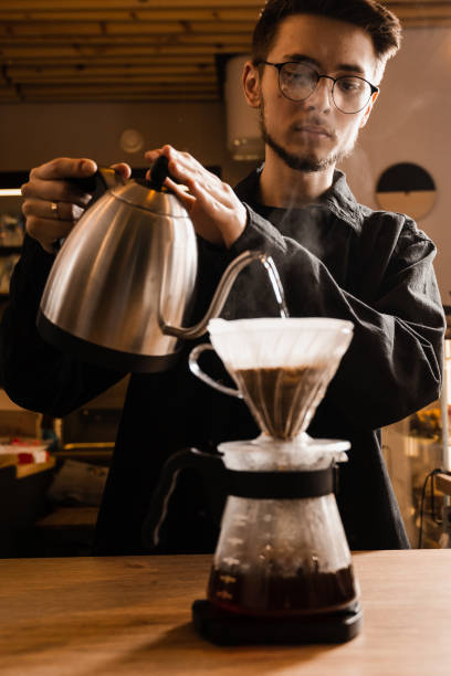 istock Pour over filter coffee alternative brewing method. Barista is pouring hot water over roasted and ground coffee beans contained in paper filter. 1473047319