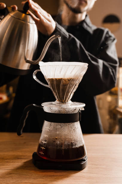 istock Pour over filter coffee alternative brewing method. Barista is pouring hot water over roasted and ground coffee beans contained in paper filter. 1473048232