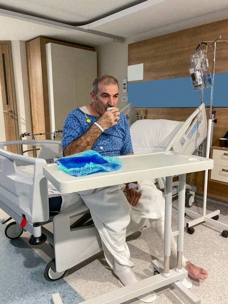 paciente masculino sentado en la cama del hospital y está bebiendo agua en la sala del hospital - 16022 fotografías e imágenes de stock