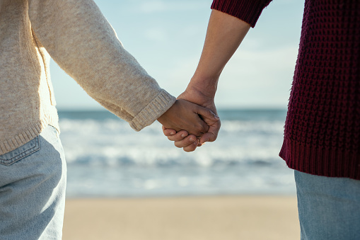 Close up of beautiful couple holding hands while walking in a cold winter on the beach.