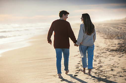 Portrait of beautiful young couple in love walking together in a cold winter day on the beach.