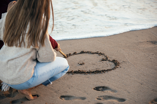 Portrait of beautiful couple in love drawing a heart in the sand with a stick enjoying the day on the beach.