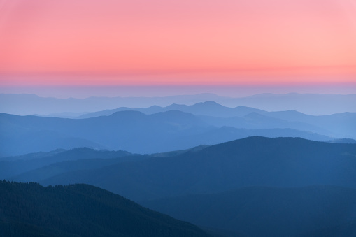 Amazing silhouettes of a mountains at colorful sunset in summer in Ukraine. Landscape with mountain ridges in fog, pink sky in the evening. Nature background. Hills at twilight. Scenery