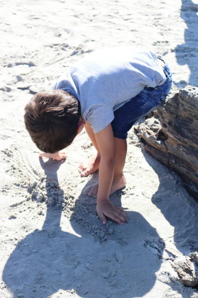 istock 4-year-old boy dressed and barefoot playing with the sand on the beach. 1473053784