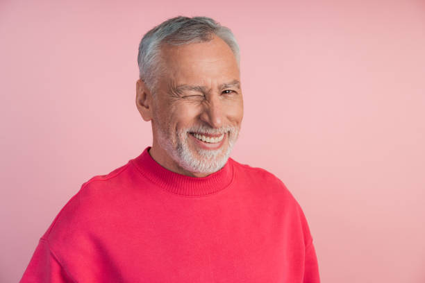 istock Curious, senior man in a bright pullover winks on a pink background. Attractive man flirts on a copy space. 1473055198