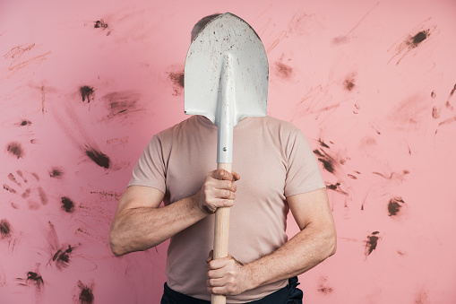 Man hid behind a shovel on a pink background. The concept of housekeeping, farming, gardening
