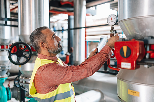 A mature Caucasian male engineer is checking the pressure in a heating plant.