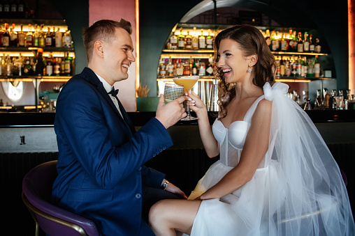 bride and groom inside a cocktail bar in a bright atmosphere with a glass of drink