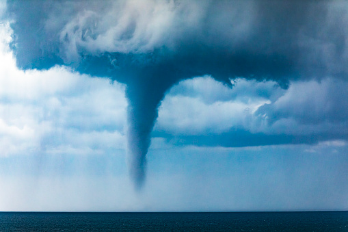 Tornado waterspout in the ocean off the coast with dark dramatic sky, clouds and windy ocean