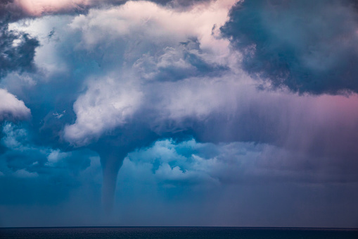 Tornado waterspout in the ocean off the coast with dark dramatic sky, clouds and windy ocean