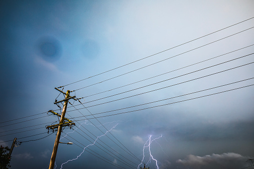 Storm with rainbow and dark dramatic sky, clouds over power lines and electricity poles. Extreme weather scene in urban Australia.