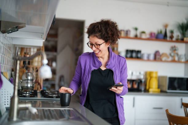istock Woman using mobile phone and having a coffee in the kitchen 1473065009